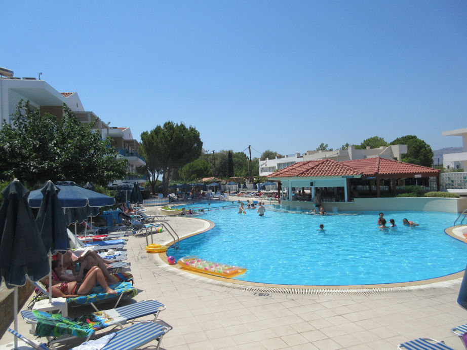 Pefki Islands hotel pool area with peopl swimming and sunbathing around the edge. Click Here to go the package holidays page.